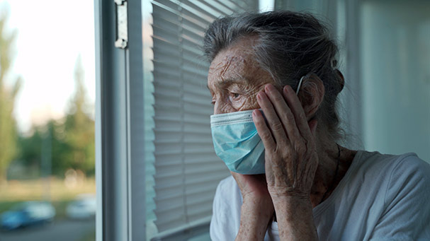 Sad elderly female looking out window of nursing home.